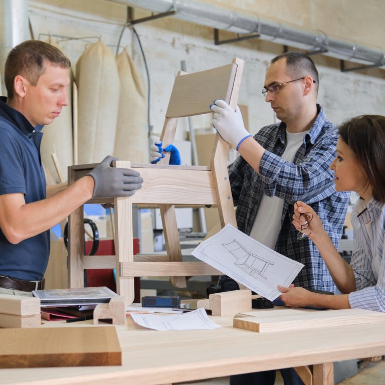 Group of working designers discussing production of new model of wooden modern chair, background carpentry workshop